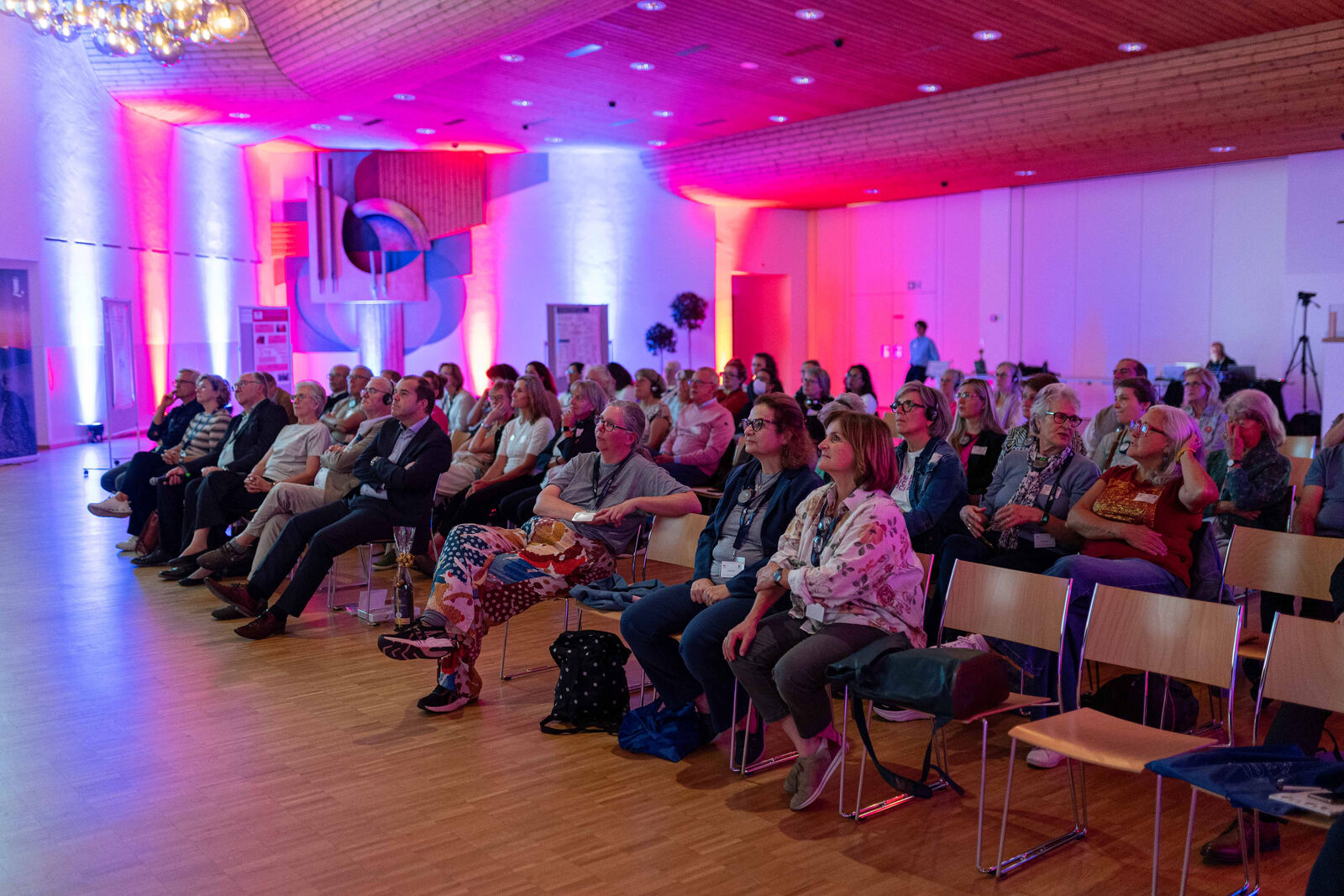 The audience in a hall lit in pink and blue